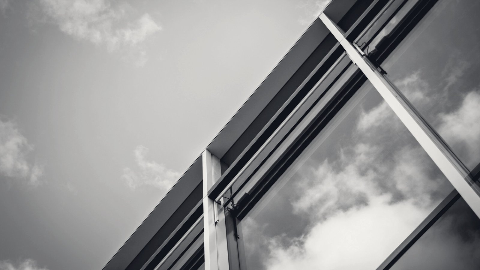 A glass curtain wall angled upward against overcast sky.