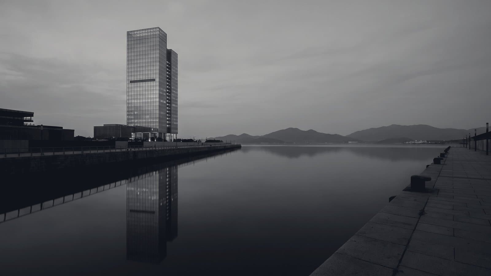 A single glass tower on a still harbor at dusk, mirrored in flat black water.