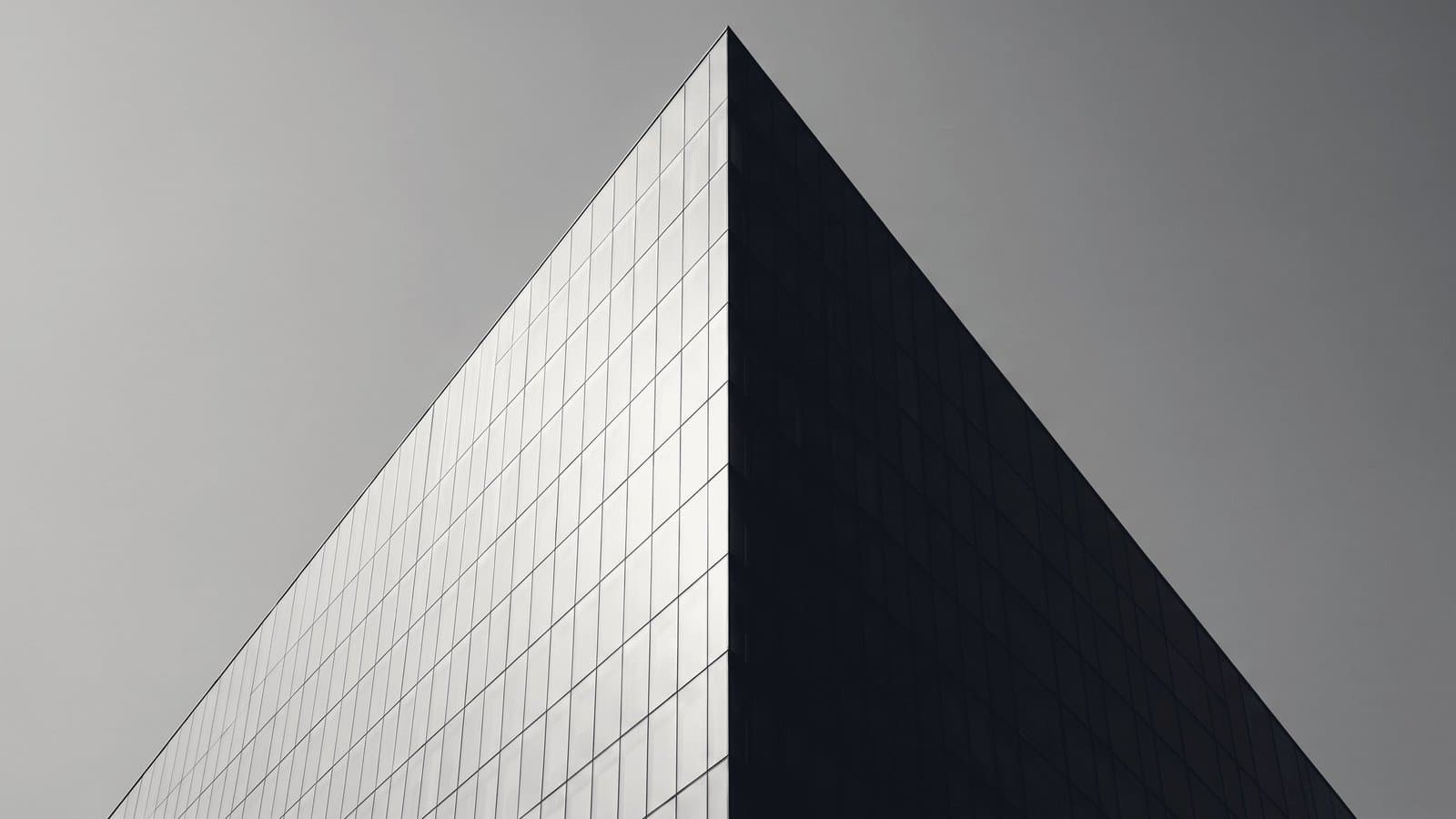 The corner of a glass office tower, one face in hard light and the other in deep shadow.